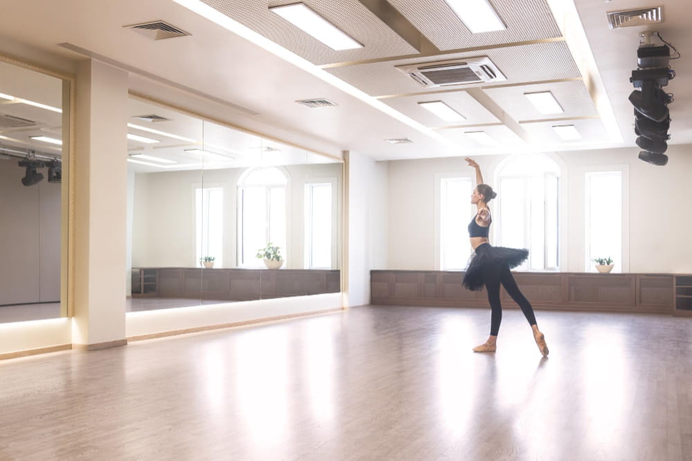 Une ballerine en tutu noir s'exerce à la danse classique dans un studio lumineux avec de grands miroirs